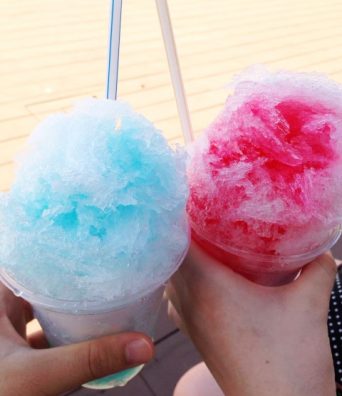Two hands “clink” their servings of shaved ice together.