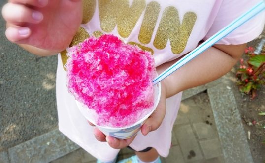 A young girl holds a serving of fluffy Hawaiian shave ice to the camera.