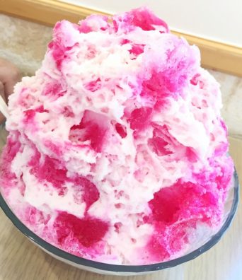 A close up of a large and fluffy serving of pink Hawaiian shave ice.