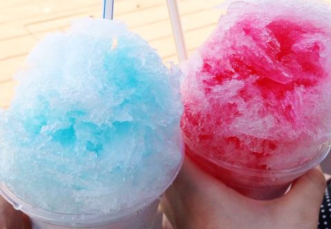 Two hands “clink” their servings of shaved ice together.