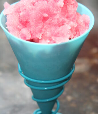 Reddish pink Hawaiian shave ice is served in a plastic cone.